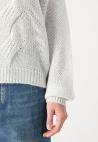 Világosszürke kötött pulóver, laza szabással, bordázott mandzsettákkal és texturált mintával. Látható varrásokkal és kényelmes illeszkedéssel rendelkezik.