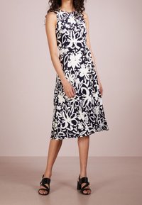 Abito floreale blu navy con motivi astratti bianchi, design senza maniche, gonna svasata e un fiocco in vita. Sandali neri con tacco a blocco.