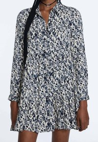 Leoprint-Kleid in Creme, Marineblau und Grau. Mit knöpfbarer Vorderseite, langen Ärmeln und einem gestuften Rock mit lockerem Schnitt. Weiches Material.