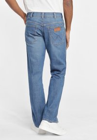 Jeans de mezclilla azul con corte recto, cinco bolsillos y una parche de piel marrón en la parte posterior de la cintura. Acabados con detalles cosidos.