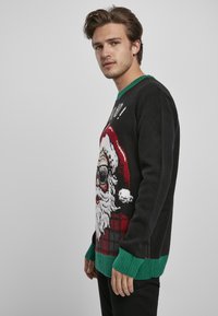 Pulover de Crăciun negru cu un design festiv al feței lui Moș Crăciun, guler și manșete ribbate verzi, cu accente în carouri roșii și negre.