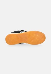 Schwarze Sportschuhe mit einer orangefarbenen, strukturierten Gummisohle, die ein geschwungenes Design aufweisen und kontrastierende weiße Akzente im Obermaterial haben.