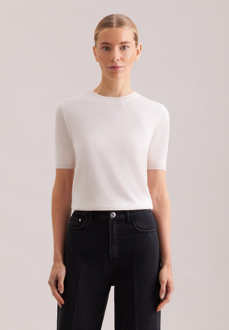 Top bianco a maniche corte in maglia con scollo rotondo, abbinato a jeans di denim neri a vita alta con bottone e tasche. Tessuto liscio.