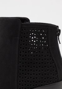 Stivaletto nero alla caviglia con motivo a triangoli perforati, texture in camoscio e zip laterale, caratterizzato da un tacco e una finitura neri.