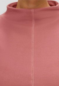 Vaaleanpunainen ribattu kauluspaidan malli, jossa on keskeinen sauma. Pehmeä kangas, jossa on sileä tekstuuri, ja se korostaa vartalon myötäistä muotoilua.