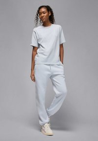 T-shirt in cotone grigio chiaro e pantaloni della tuta abbinati, caratterizzati da una vestibilità rilassata e vita elastica, abbinati a scarpe sportive chiare.