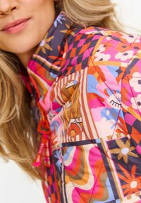 Kurtka pikowana z wielokolorowym wzorem kwiatowym i geometrycznym w odcieniach różu, pomarańczu i niebieskiego, z wysokim kołnierzem i detalem z regulowanym sznurkiem.