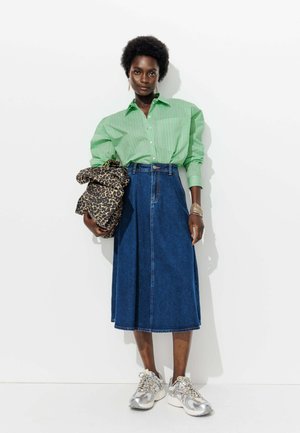 Chemise à rayures vertes, jupe en denim, sac en imprimé léopard et baskets argentées, stylées avec des bracelets empilés. Textures et formes simples.