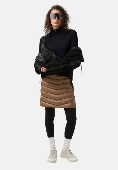 Czarna bluzka na zamek, puchowa czarna i brązowa kurtka, brązowa spódnica puchowa, czarne legginsy, białe skarpetki, beżowe chunky sneakers oraz lustrzane okulary przeciwsłoneczne.