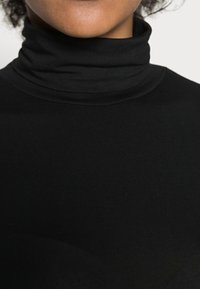 Crni turtleneck top izrađen od rastezljivog materijala, sa prilagođenim dizajnom i glatkom teksturom, te visokim ovratnikom.