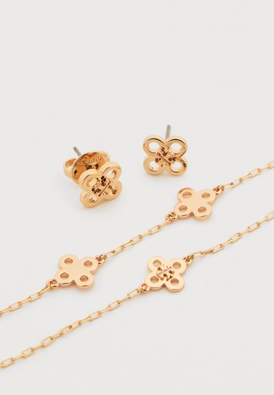 Σκουλαρίκια καρφάκια σε χρυσό τόνο και κολιέ με αλυσίδα που ταιριάζει, με μοτίβα σε σχήμα τετράφυλλου τριφυλλιού σε λευκό φόντο.