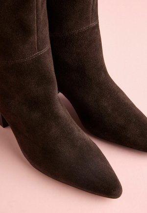 Juodos zomšinės kulkšninių botai su smailu pirštu, tekstūruota paviršiumi ir vidutiniu blokuotu kulnu. Yra matomi siūlės iš šonų.