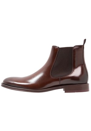 Brązowy skórzany but Chelsea z elastycznymi panelami po bokach, zaokrąglonym noskiem, gładkim wykończeniem i niskim, warstwowym obcasem. Klasyczny design o wysokości do kostki.