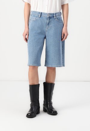 Light blue denim shorts with a relaxed fit, ending just above the knee, paired with knee-high black leather boots featuring zippers.