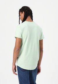 Miętowa, krótko rękawowa koszulka z zaokrąglonym dołem i podwiniętymi rękawami. Wykonana z miękkiej tkaniny, z minimalnymi detalami szwów.