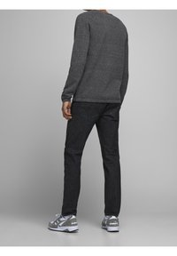 Szara koszula z długim rękawem, ciemne dżinsy i szare trampki z białymi akcentami. Strój ma swobodny fason, dopasowany kształt i teksturowany materiał.