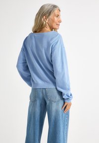 Pull en tricot bleu clair à coupe décontractée, avec des manches larges et un ourlet côtelé, associé à un jean en denim délavé taille haute.