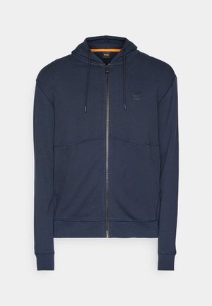 Sweatshirt azul marinho com fecho éclair, feito de um tecido macio, apresentando um capuz com cordão, costuras texturizadas e um pequeno emblema no peito.