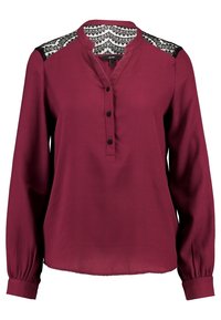 Blouse bordeaux à manches longues avec panneaux en dentelle noire sur les épaules, encolure sans col et trois boutons noirs sur la patte de boutonnage avant.