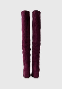 Bocanci din suede violet, până la genunchi, cu un finisaj texturat, având toc bloc și detalii cu fermoar pe spate pentru a fi ușor de purtat.