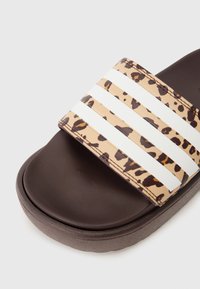 Slide sandal with a leopard print strap featuring three white stripes, dark brown footbed, and textured sole. Soft, flexible material.