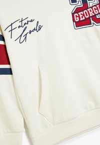Sudadera de algodón en color crema con detalles en rojo y azul. Presenta "Future Goals" bordado en azul marino y un gran estampado "GEORGIA 22".