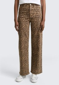 Pantalones de pierna ancha con estampado de leopardo en marrón y negro. El tejido parece suave con una textura lisa. Combinados con zapatillas blancas.