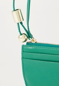 Green leather wallet featuring a textured finish, zip closure, and a gold-tone hardware accent for strap adjustment.