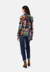 Long-sleeve shirt with a multicolored floral and animal pattern, made of a soft fabric. Paired with loose denim jeans and brown heeled boots.