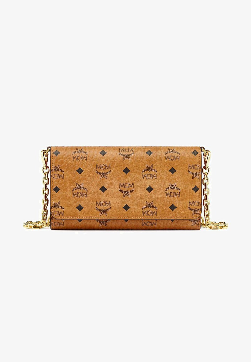 Sac à main en cuir tan avec une chaîne dorée, orné de logos MCM noirs répétés et de motifs en diamants. Texture lisse avec fermeture à rabat.