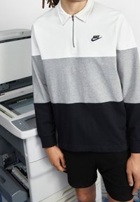Nike zip-up långärmad tröja i vita, grå och svarta färgblock med krage. Har en liten, svart logotyp på bröstet.
