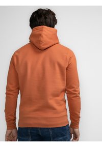 Felpa arancione in cotone con vestibilità comoda, dotata di un ampio cappuccio, maniche lunghe e polsini e fondo a costine. Tessuto semplice, senza motivi visibili.