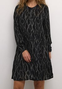 Robe noire à manches longues, col rond, avec un motif de lignes ondulées. Détail de boutons à l'avant et jupe fluide à volants.