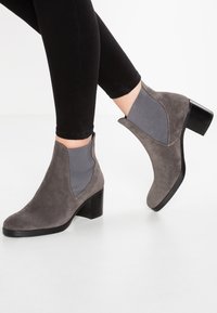 Szare zamszowe botki za kostkę z kontrastującą szarością elastyczną boczną wkładką, zaokrąglonym noskiem i niskim obcasem typu słupek. Gładka tekstura i przeszycia.