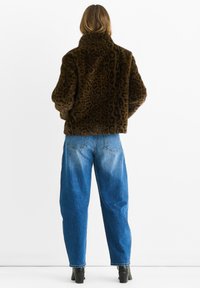 Giacca in finta pelliccia marrone con stampa leopardata, colletto alto e vestibilità ampia, abbinata a jeans in denim blu chiaro a vita alta e stivaletti neri.