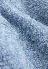 Gros plan sur un tissu polaire bleu clair doux et bouclé montrant sa surface texturée, duveteuse et ses plis délicats.