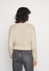 Pull côtelé beige avec un col rond, des manches longues et une coupe courte. Porté avec un jean taille haute gris foncé, mettant en valeur un tissu texturé.