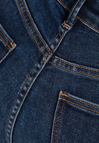 Mörkblå denimtyg med synliga sömdetaljer och två framfickor. Texturen är något sliten, vilket framhäver tygets hållbarhet.