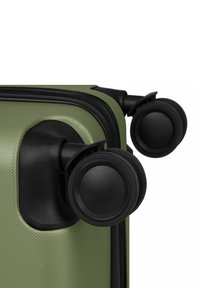 Deux roues double spinner noires fixées à un coin de valise verte texturée avec un bord de fermeture éclair noir.