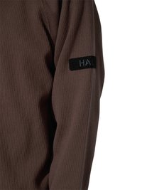 Brązowy prążkowany długi rękaw z czarną prostokątną naszywką na górnej części rękawa, częściowo ukazującą litery "HA".