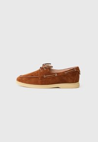 Brown suede lace-up boat shoes with a rounded toe, tan rubber sole, metal eyelets, and decorative stitching along the upper.