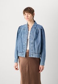 Denim bomber jakna u svijetlo plavoj boji s opuštenim krojem, dugmadima na pritisak i detaljima napučenih ramena, u kombinaciji s smešnim suknjom.