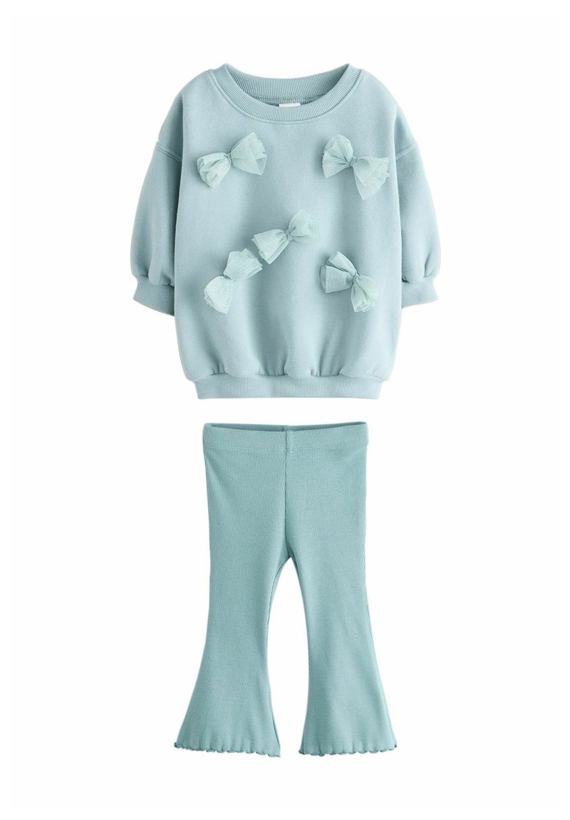 Lyseblå sweatshirt med puffede ærmer og dekorative sløjfer. Ribbede lyseblå flared leggings. Blødt stof med en struktureret overflade.