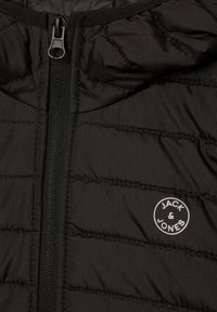 Black padded jacket with a zip front, featuring a circular logo "JACK & JONES" in white. The fabric has a smooth texture and quilted pattern.
