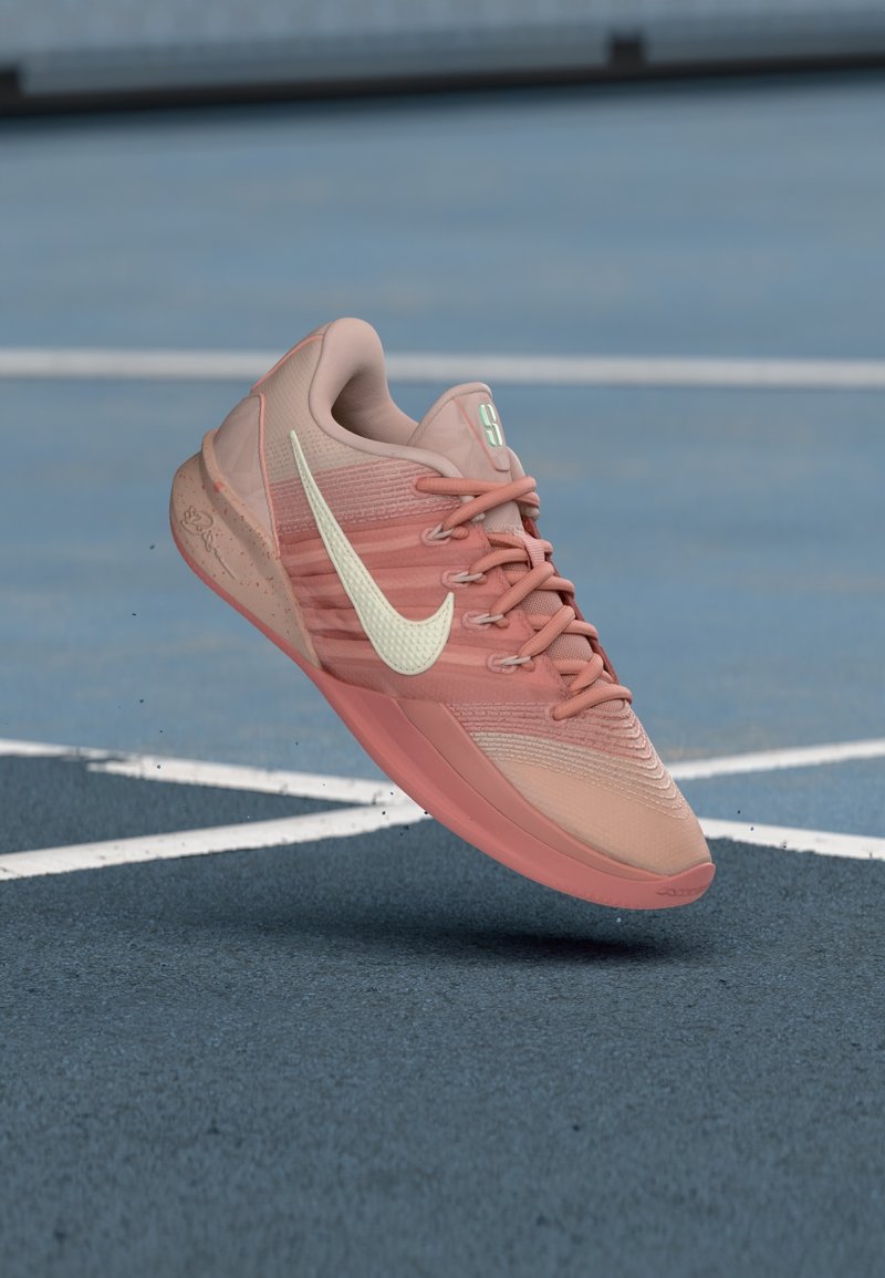 Chaussure de sport Nike rose en l'air au-dessus de la surface bleue d'un court de tennis avec des lignes blanches visibles.
