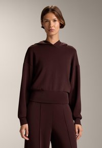 Burgundowa bluza z kapturem, z długimi rękawami, o luźnym kroju i ściągaczu. Gładka tekstura z minimalnymi detalami. W zestawie ze spodniami w tym samym kolorze.