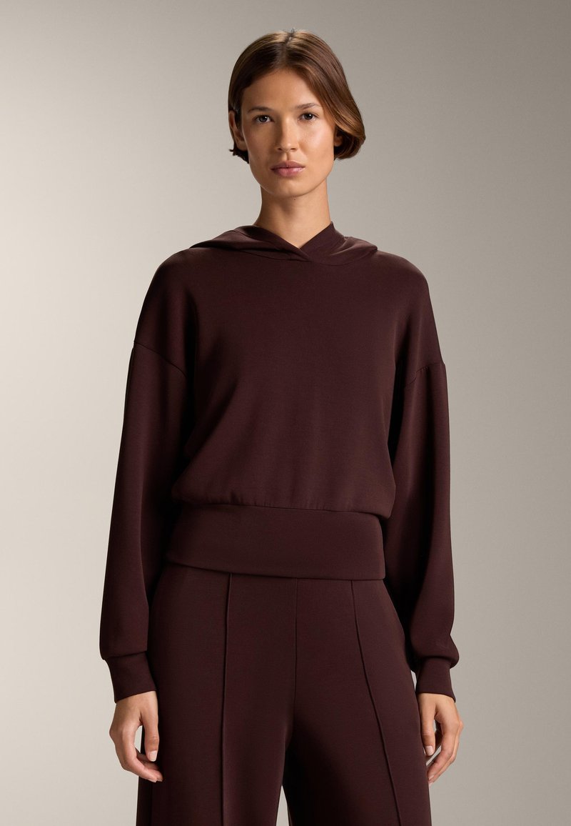 Burgundowa bluza z kapturem, z długimi rękawami, o luźnym kroju i ściągaczu. Gładka tekstura z minimalnymi detalami. W zestawie ze spodniami w tym samym kolorze.