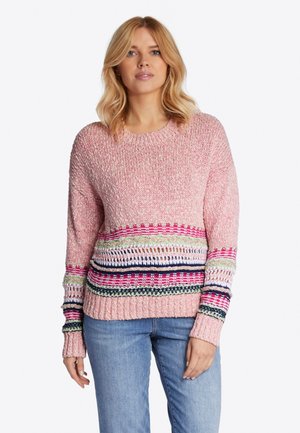 Rosa gestrickter Pullover mit bunten horizontalen Streifen an der Taille und den Ärmeln. Lange Ärmel und gerippte Bündchen. Getragen mit blauen Jeans.