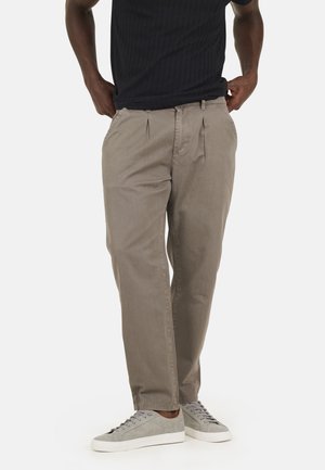 Pantalons gris clair avec des plis, fabriqués à partir d'un tissu doux. Présente une coupe décontractée et des poches latérales. Associés à des baskets grises.