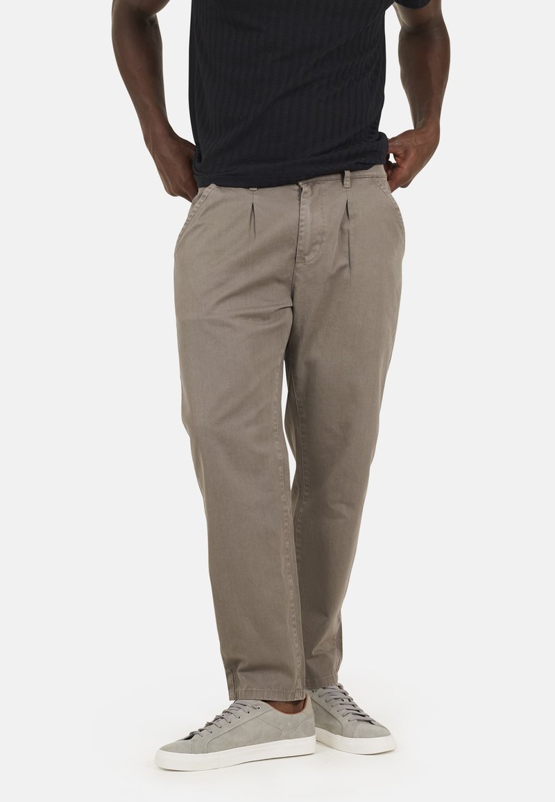 Pantaloni grigi chiari con pieghe, realizzati in un tessuto morbido. Presentano una vestibilità rilassata e tasche laterali. Abbinati a sneakers grigie.